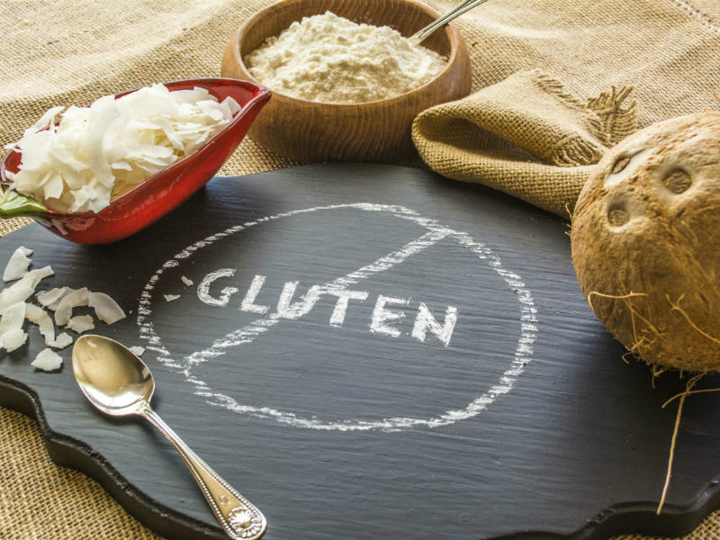 Tabla de pizarra donde aparece la palabra gluten tachada y varios sacos y cestos alrededor con productos que no pueden comer los celiacos