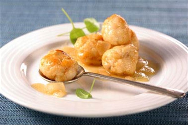 Plato blanco con cuchara de metal y albóndigas de pescado en salsa
