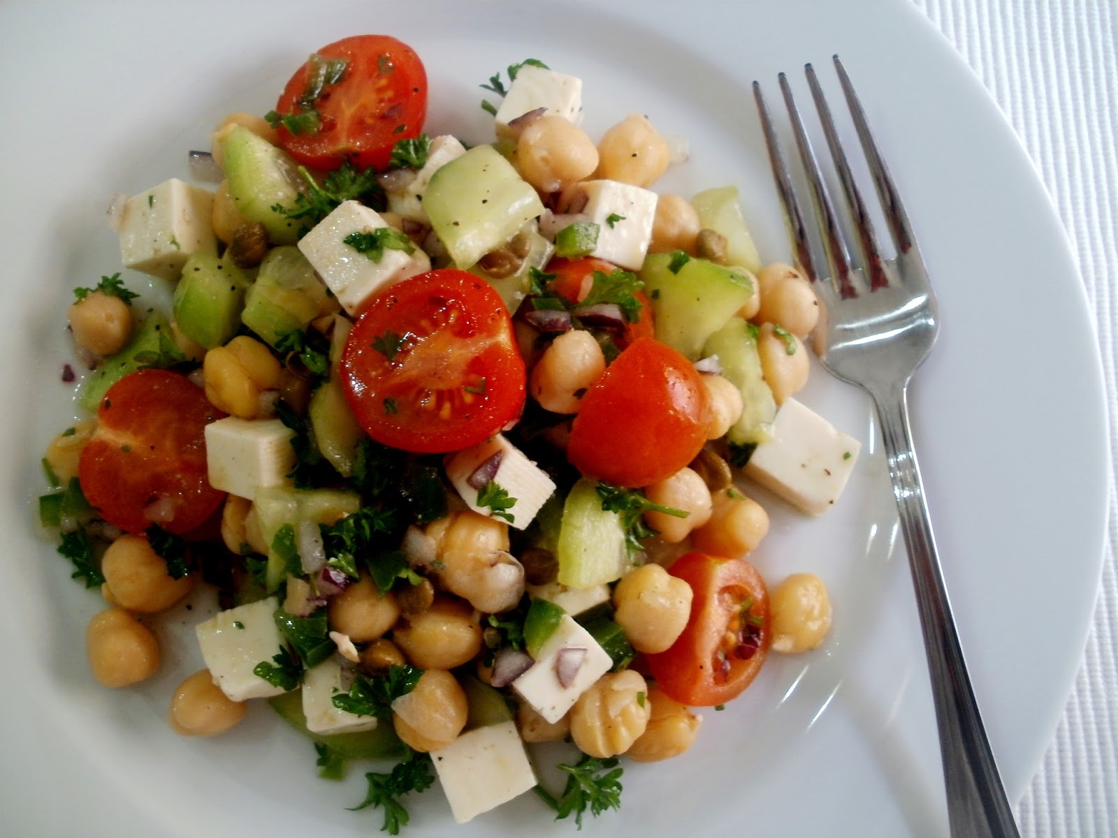 Plato blanco con tenedor de metal con ensalada de garbanzos,tomate y verduras