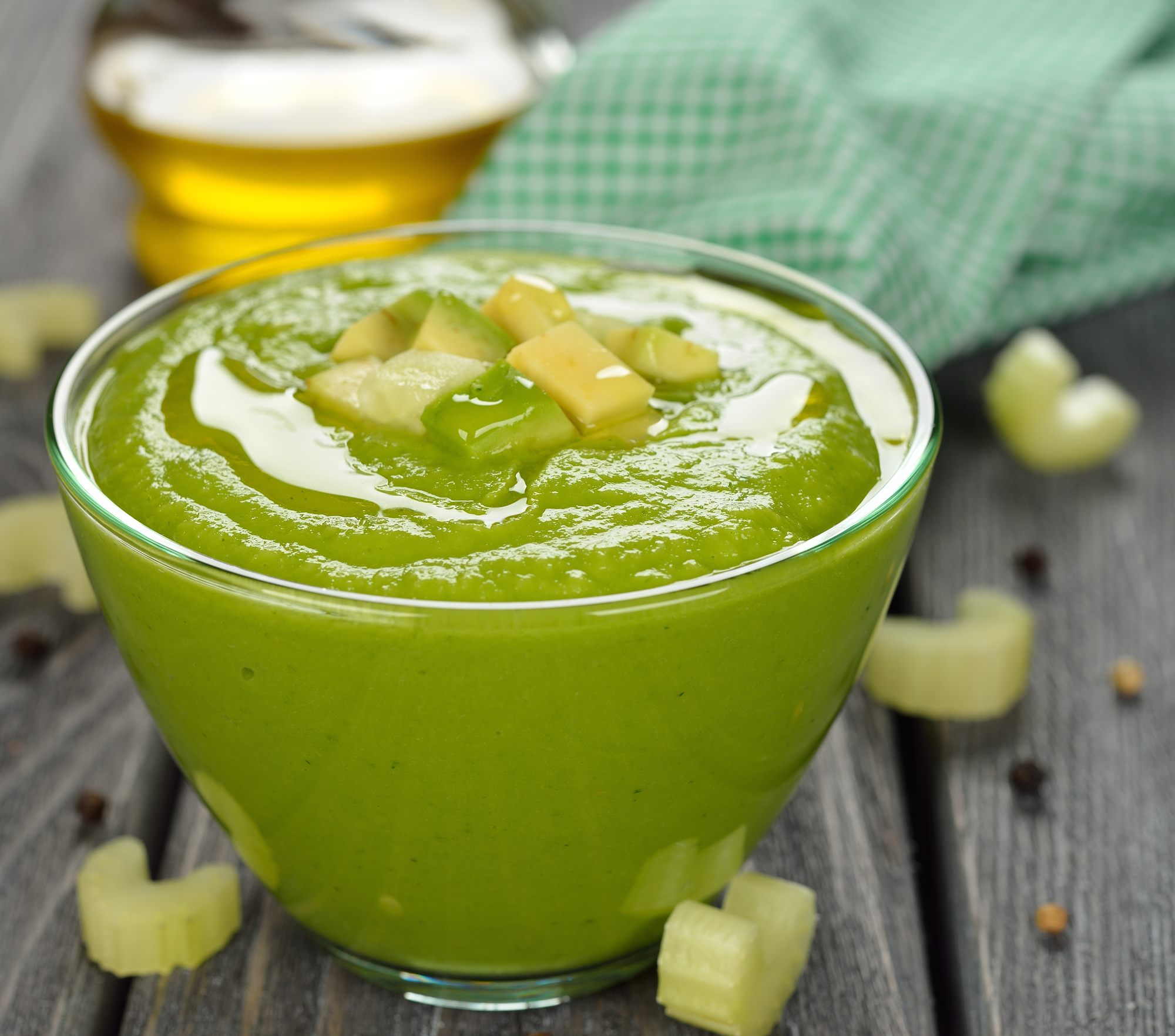 Mesa de madera negra con vaso de cristal con gazpacho verde decorado con trozos de verduras