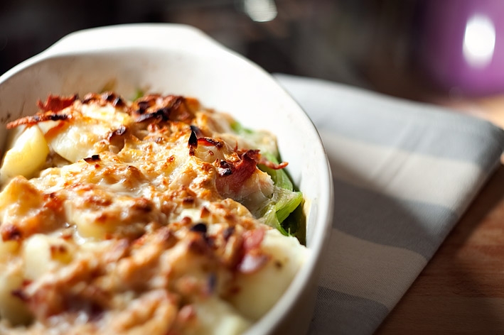 Plato blanco de borraja gratinada al horno sobre mantel a cuadros girses encima de mesa de madera
