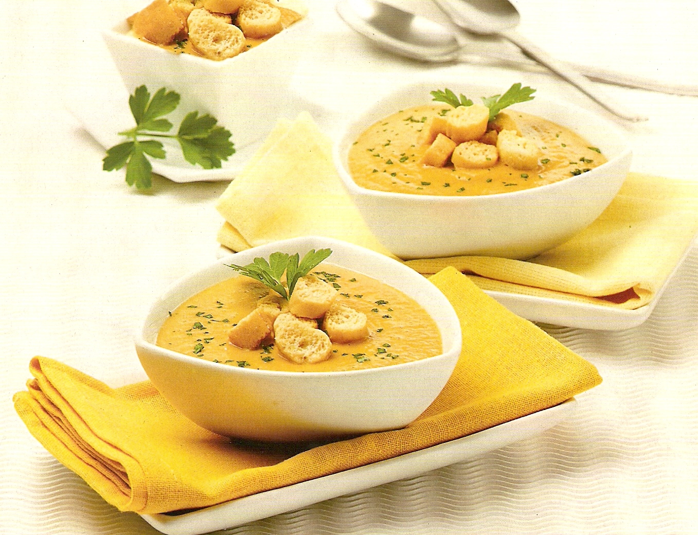 Dos platos blancos con crema de garbanzos sobre servilletas ocres encima de slavaplatos y encima de mesa con mantel blanco