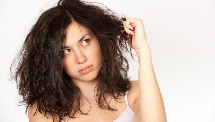 Mujer despeinada mirando su pelo con rabia