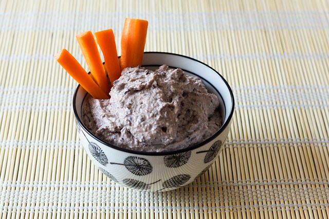 Salvamantel de bambu sobre el que aparece un bol blanco y negro con hummus de alubias rojas y crudites de zanahoria