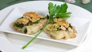 Plato blanco con lenguado con almedras y una rama de perejil en medio de ambos