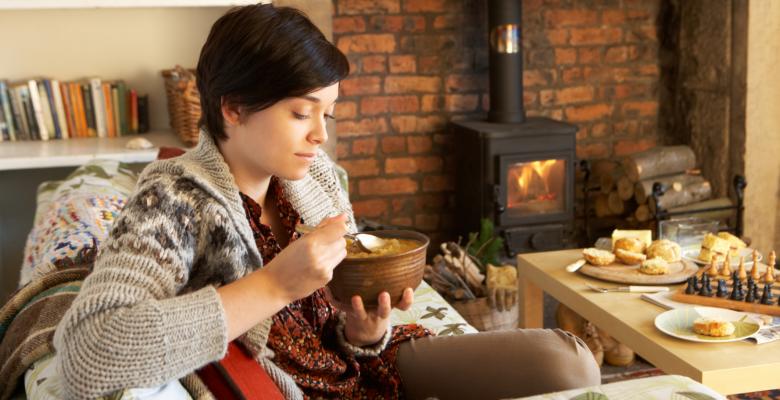 Mujer en invierno con chimenea de fondo comiendo un pure