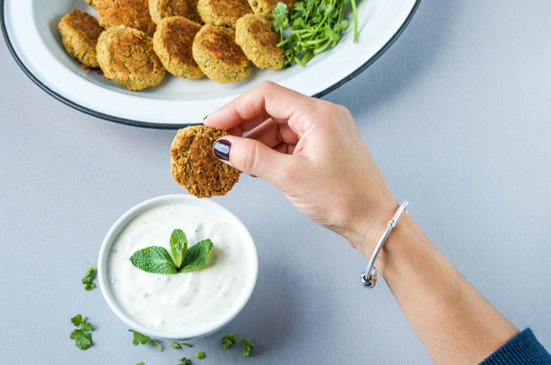 Mujer untando falafel en bol con salsa de yogur de menta