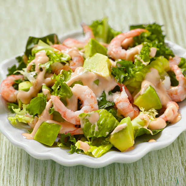 Ensalada de aguacate y gambas en plato blanco sobre mesa de madera