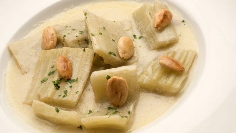 Plato blanco con cardo y salsa de almendras, almendras laminadas y perejil picado.
