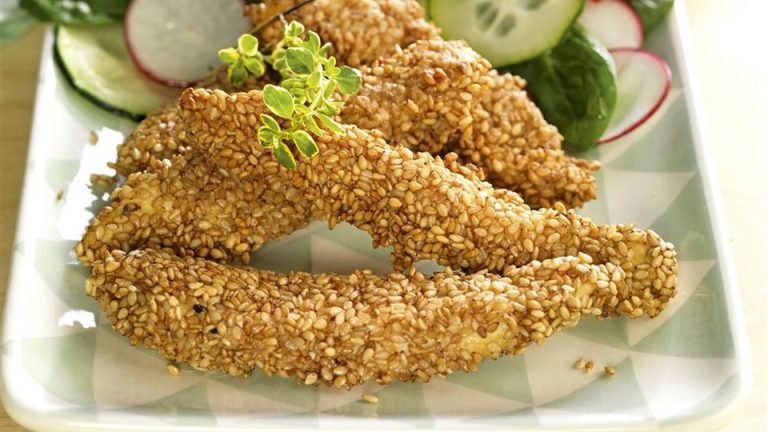 Filetes de merluza rebozada con sesamo y enslada sobre plato blanco