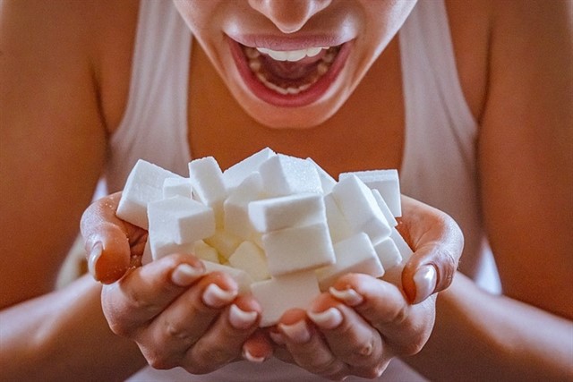 Mujer abriendo la boca queriendo comer un montón de terrones de azucar que sujeta con las manos