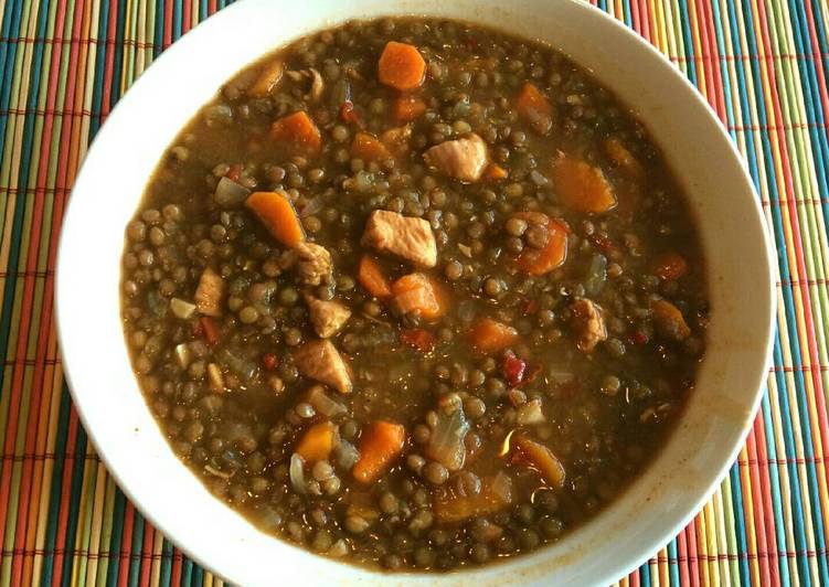 Plato blanco sobre salvamantel con lentejas con pollo y verduras
