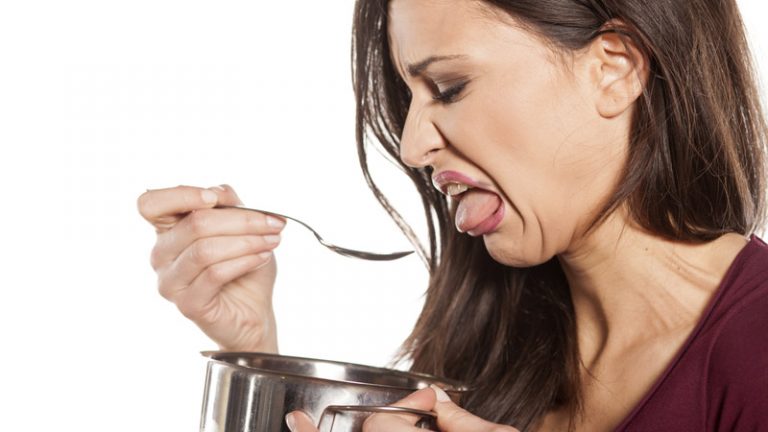 Mujer poniendo ,mala cara la chupar una cuchara y sosteniendo una cazuela