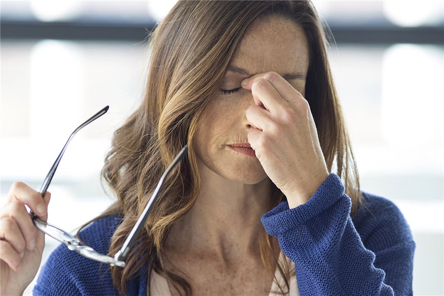 Mujer sujentando las gafas en la mano y tocandose los ojos con gesto de dolor