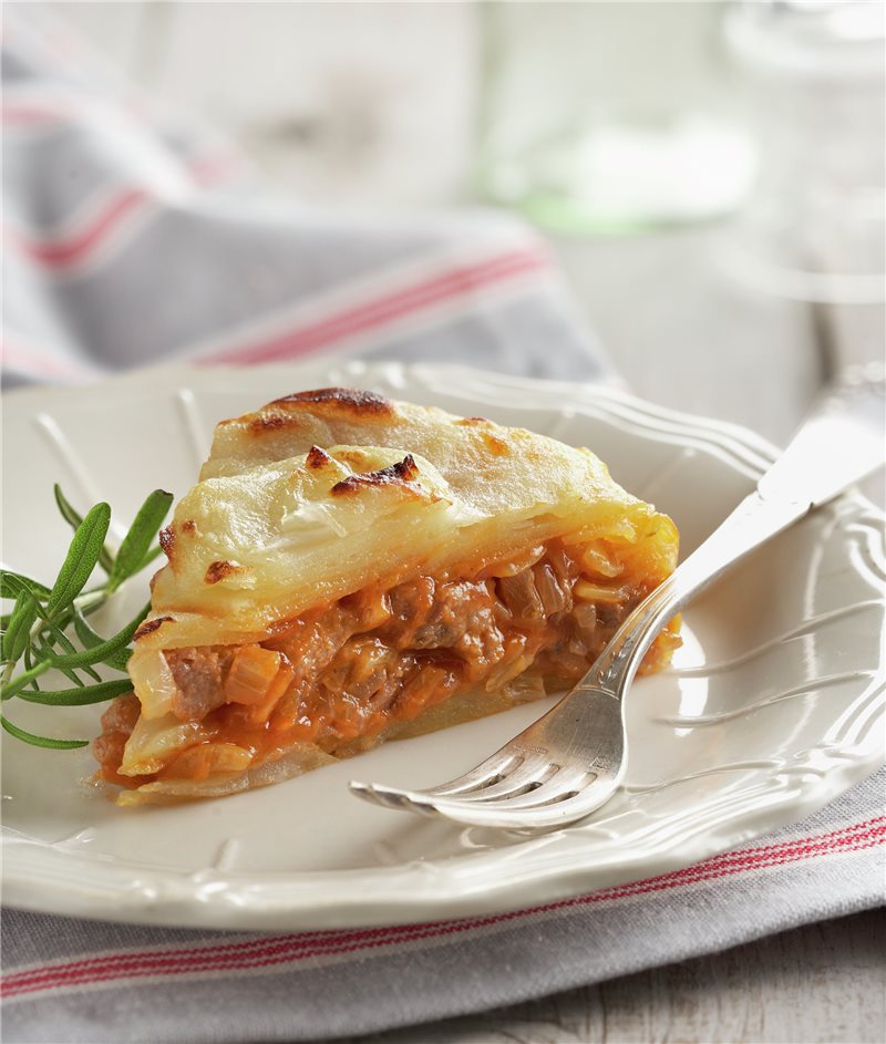 Plato blanco sonre mesa con mantel blanco con Pastel de patata, tomate y lomo de cerdo