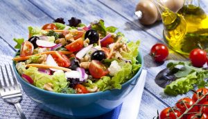 Bol azul con ensalada variada sobre mesa de madera