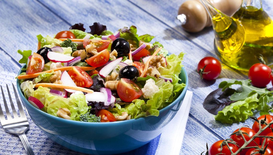 Bol azul con ensalada variada sobre mesa de madera