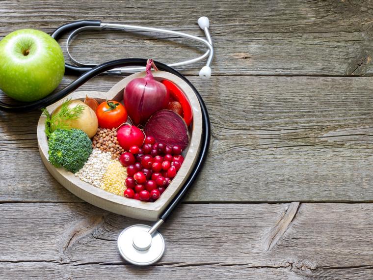 Mesa de madera y encima estetoscopio con alimentos saludables para el corazón