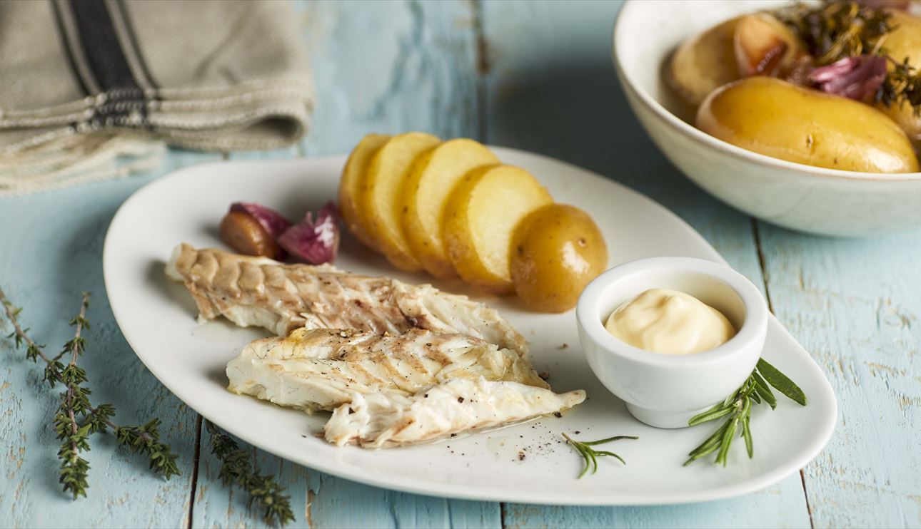 Lubina a la sal en plato blanco con guarnición de ajos y patatas