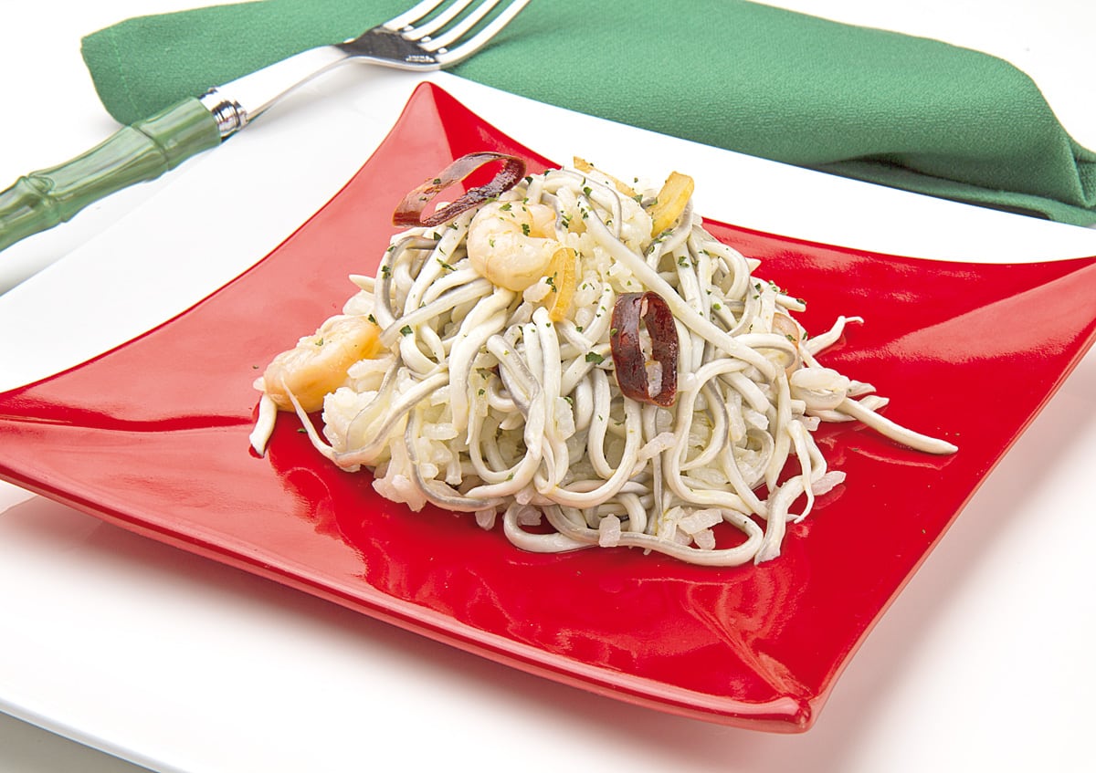 Plato rojo sobre sobreplato blanco con arroz con gulas y gambas