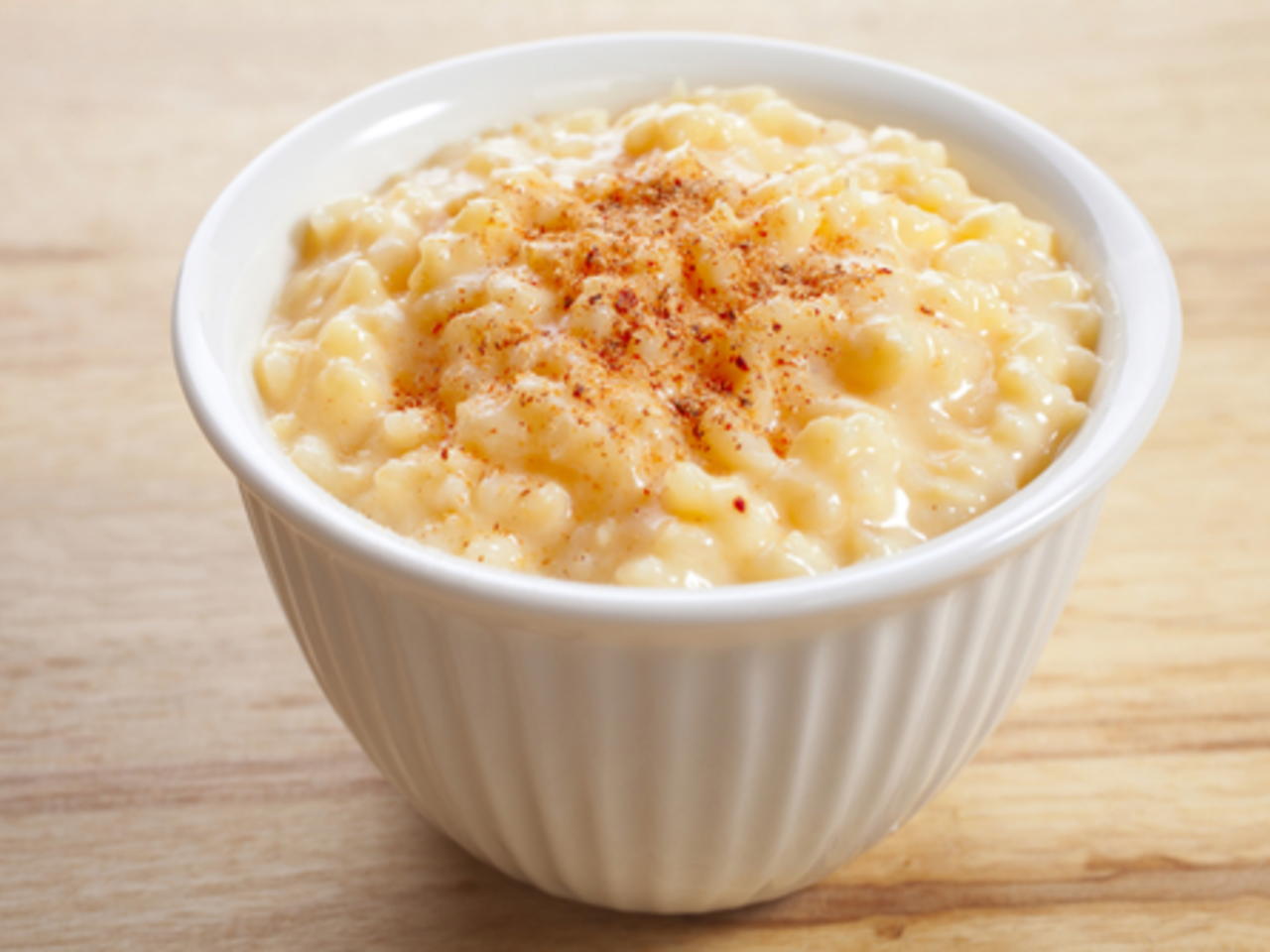 Bol blanco de arroz con leche condensada sobre mesa de madera