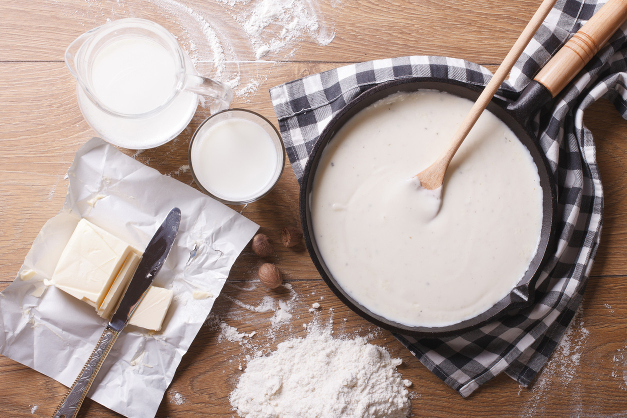 Mesa de madera con cazuela con bechamel y sus ingredientes