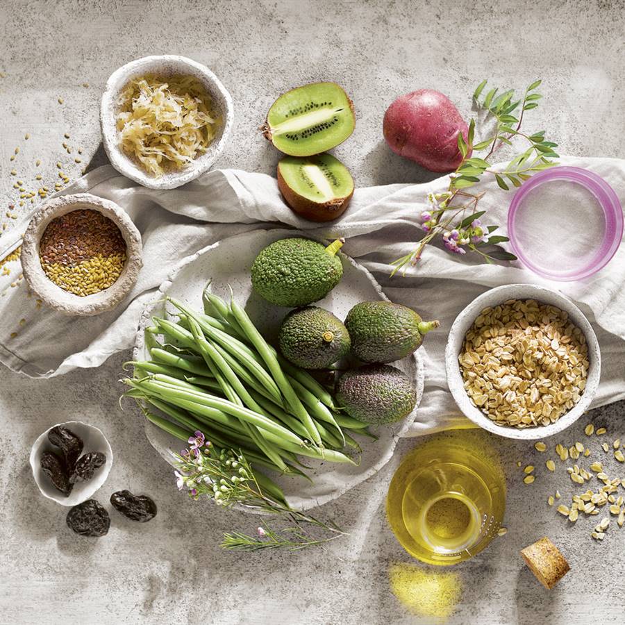 Mantel blanco y sobre él alimentos protectores de salud como aguacate, kiwis, aceite de oliva...