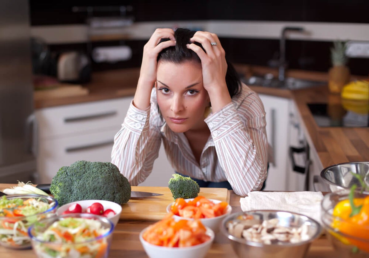 Mujer con cara de angustia sobre mesa de cocina con muchos alimentos