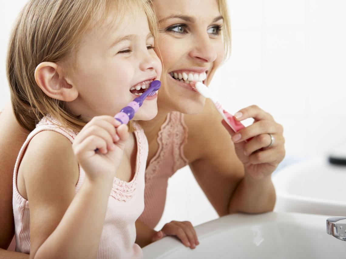 Mujer y niña pequeña frente al espejo ambas lavándose los dientes