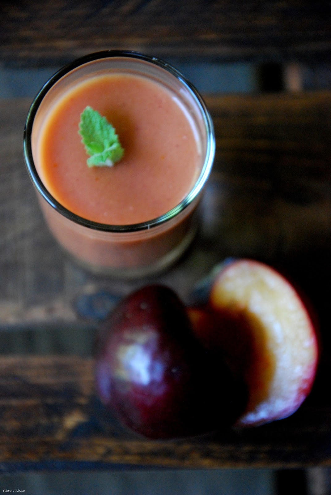 Vaso de cristal con gazpacho de ciruela roja y ciruela roja partida al lado