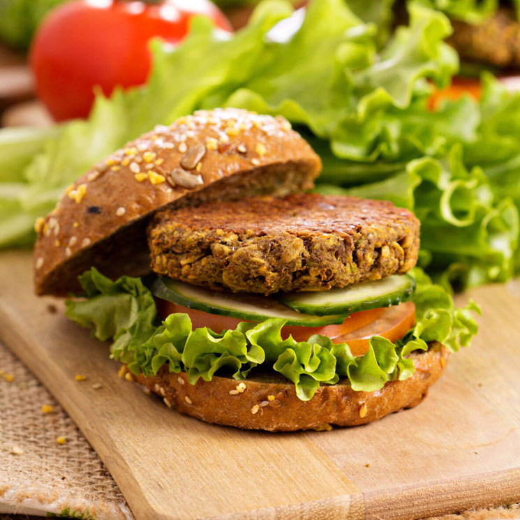 Tabla de madera y sobre ella hamburguesa vegetal con tomate , lechuga y pepino
