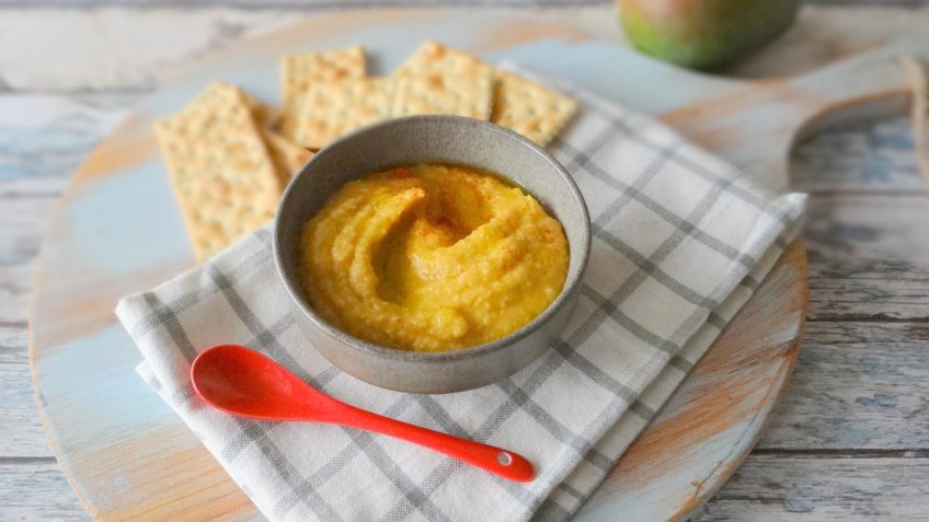 Hummus de mango en tazón blanco sobre selvilleta blanca a cuadros y cuchara roja
