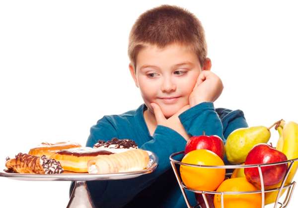 Niño mirando con deseo bollería y en otro lado fruta