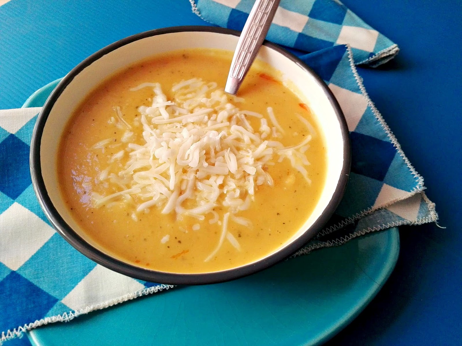 Plato de crema de vudras naranja con queso sobre plato y mantel azul
