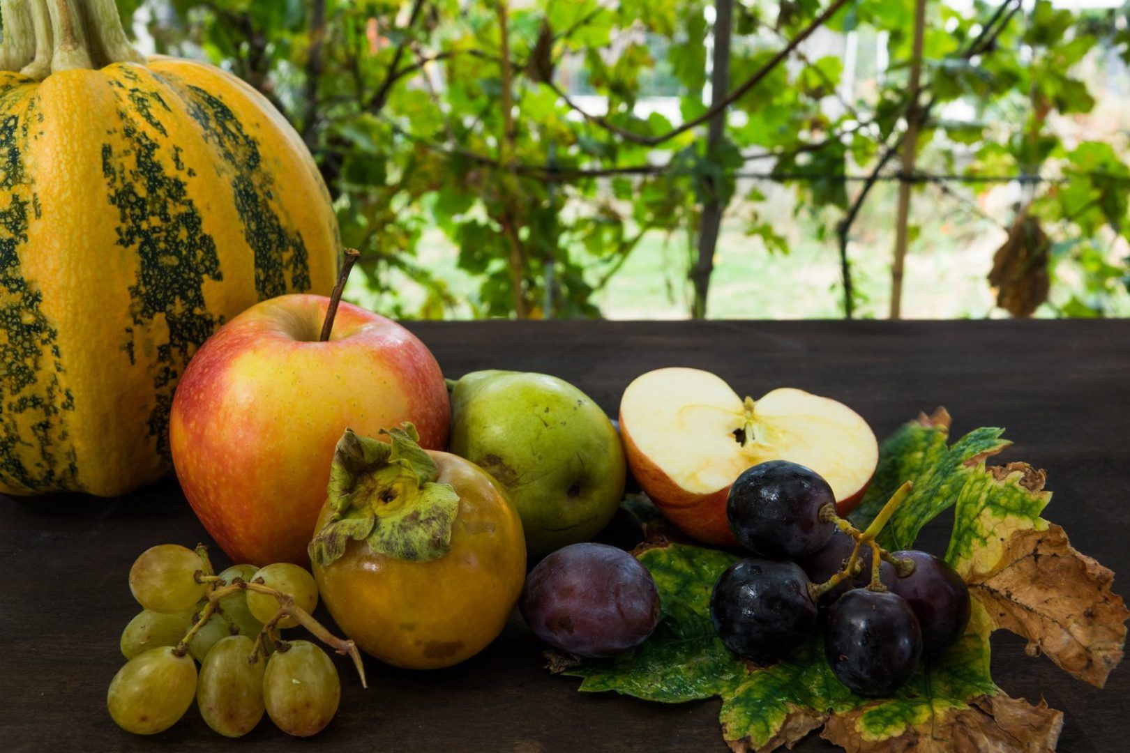 Sobre mesa de madera con jardín de fondo frutas de temporada de octubre