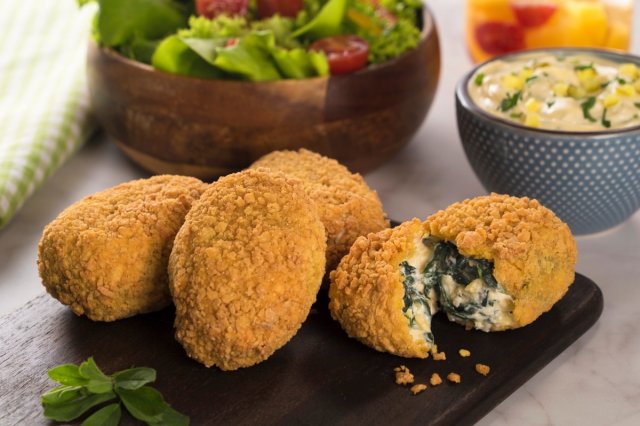 Tabla de pizarra con croquetas de espinacas y queso encima y ensalada y salsa de fondo