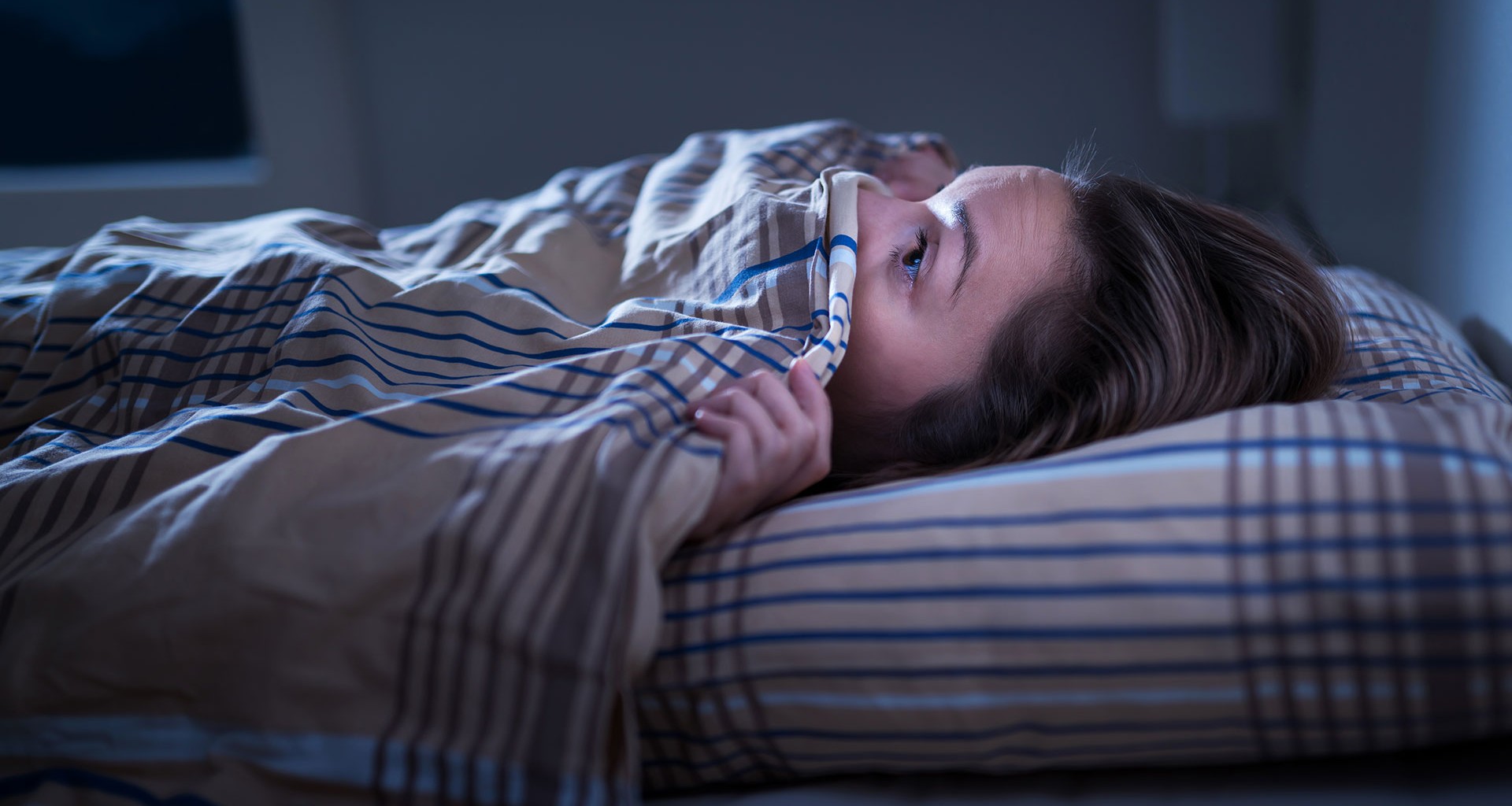 Mujer tapándose la cara en la cama con la sábana