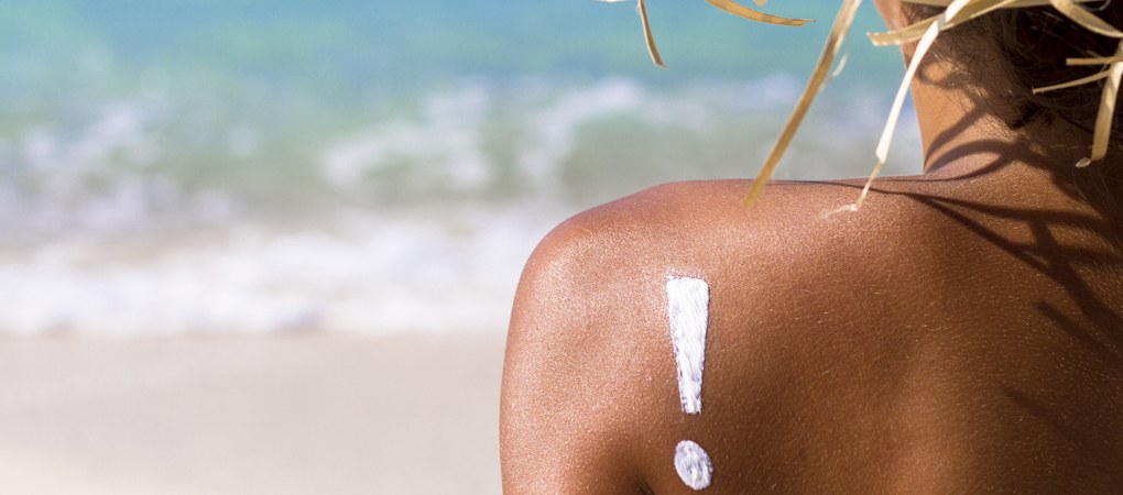 Mujer de espaldas al mar con signo de exoclamación en la espalda hecho con crema solar