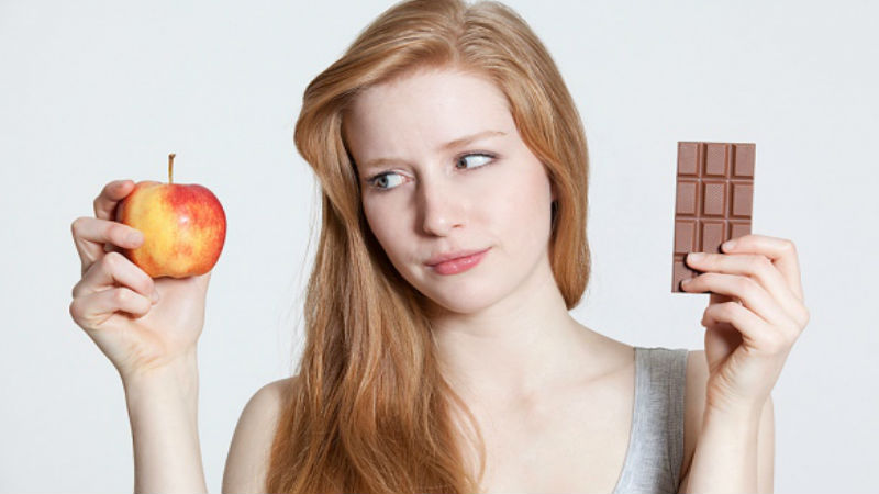 Mujer indecisa entre comer manzana o chocolate