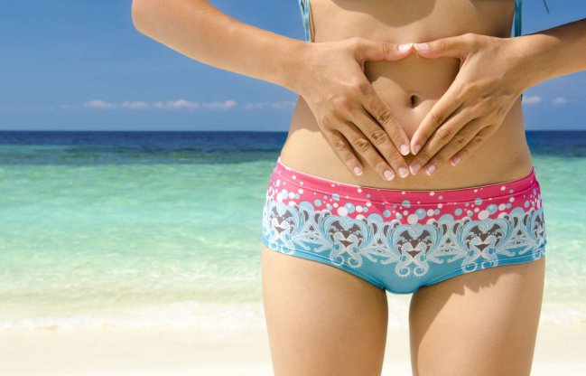 Mujer en bikini en la playa con sus manos en el vientre