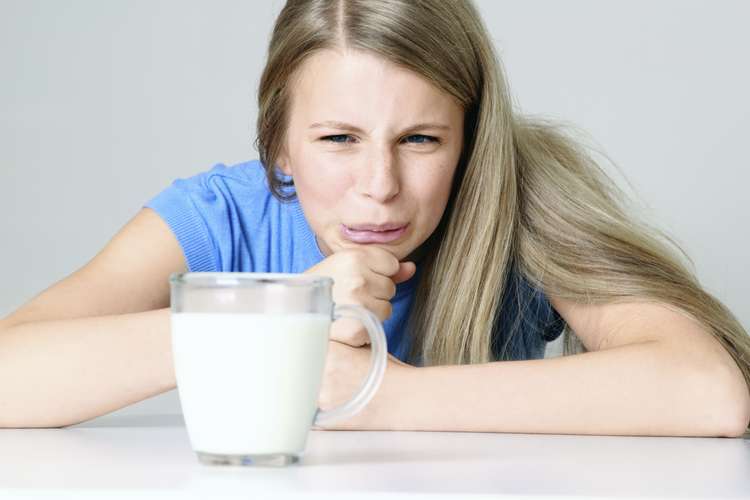 Mujer poniendo cara de disgusto al ver un vaso de leche