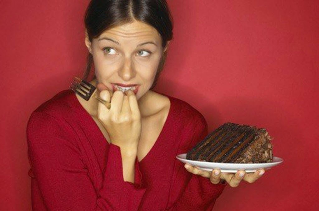Mujer vestida de rojo con dudas de comerse tarta de chocolate que tiene en la mano en un plato blanco