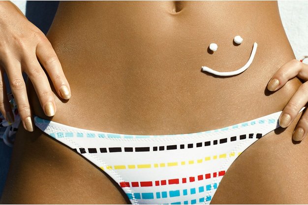 Mujer en bikini con sonrisa hecha con crema de sol en la tripa