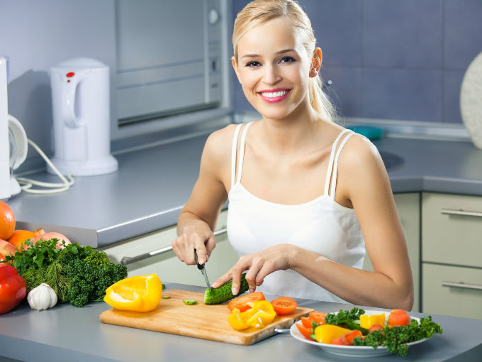 Mujer cortando verduras sonriendo en su cocina