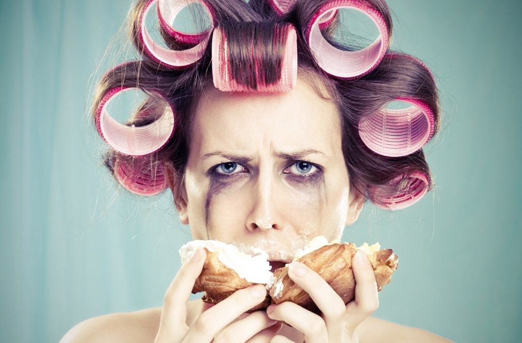 Mujer con rulos en la cabeza llorando y comiendo bollos