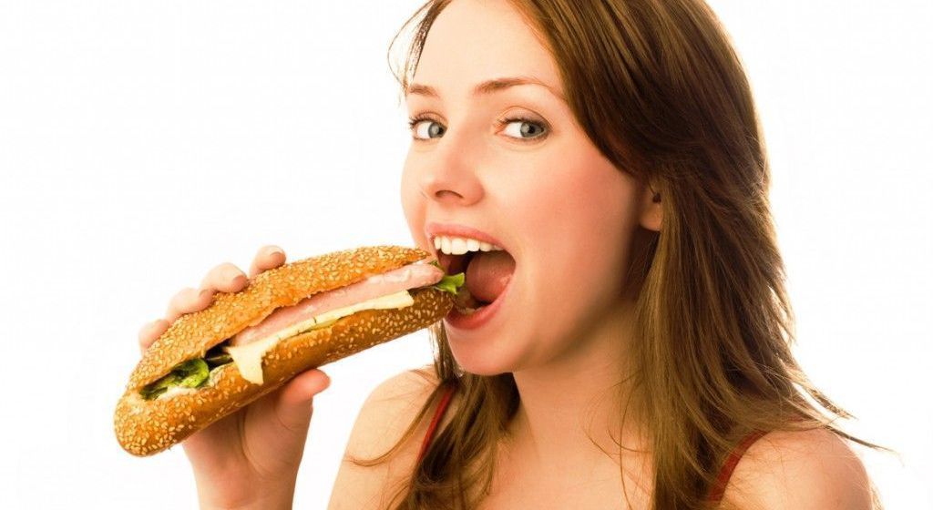 Mujer abriendo la boca para comerse un bocadillo de pan integral,pechuga de pavo,lechuga...