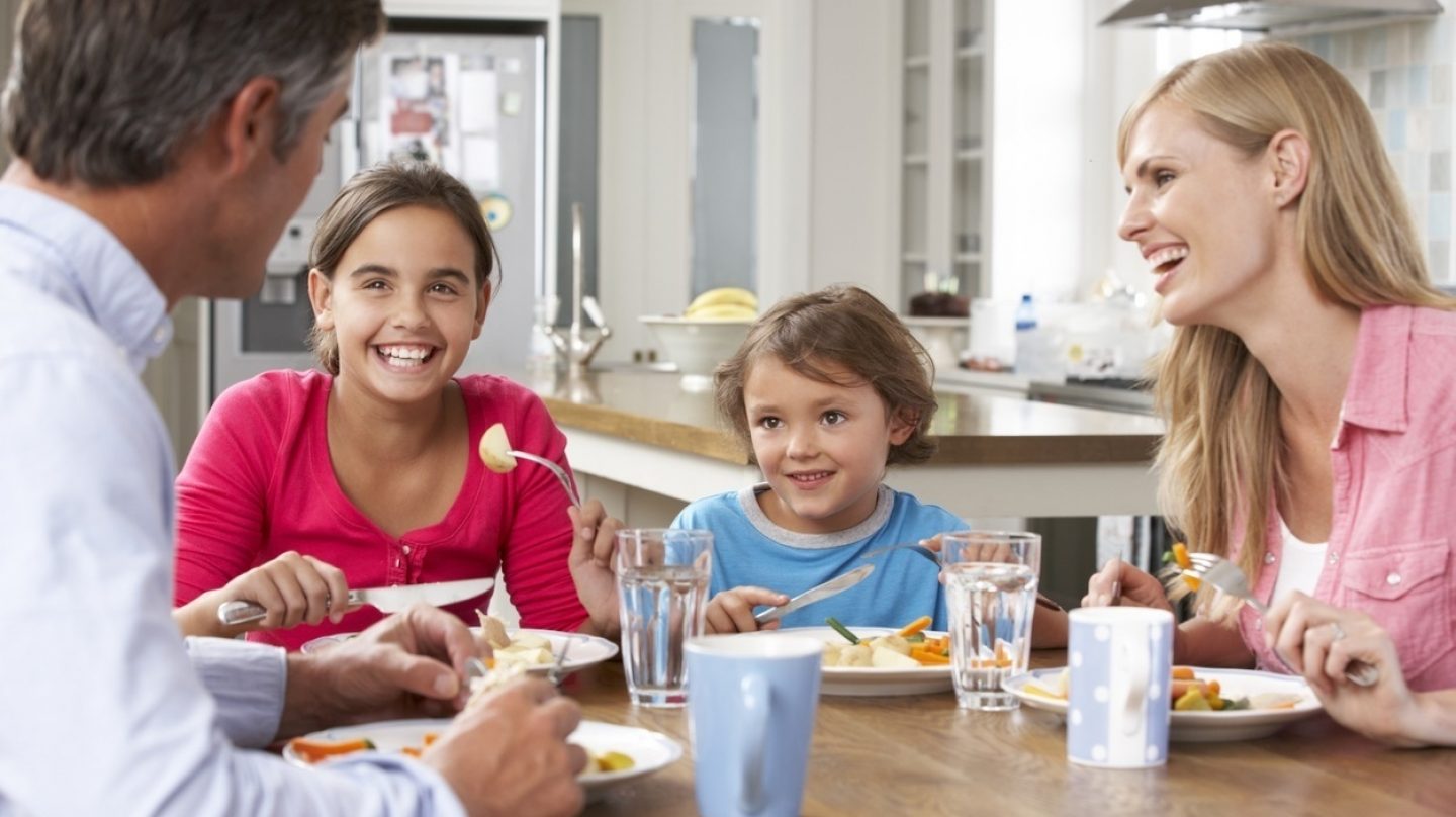 Familia de padre,madre y dos hijas comiendo en mesa de madera y sonriendo