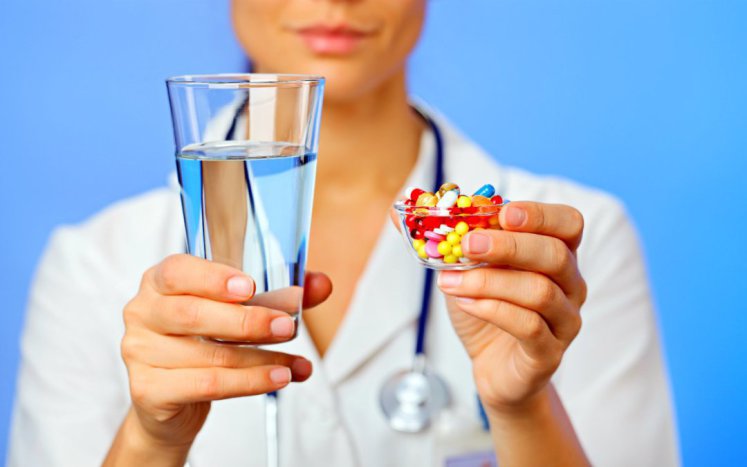 Farmaceutica con vaso de agua y en la otra mano vaso con medicamentos