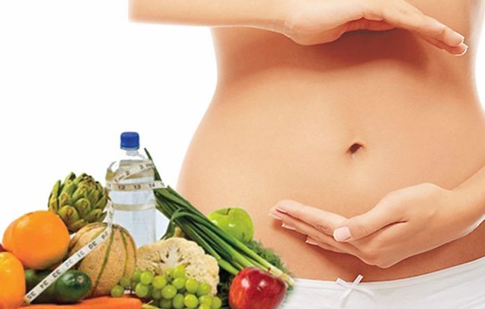 Mujer con manos alrededor del estómago y de fondo frutas, verduras y agua