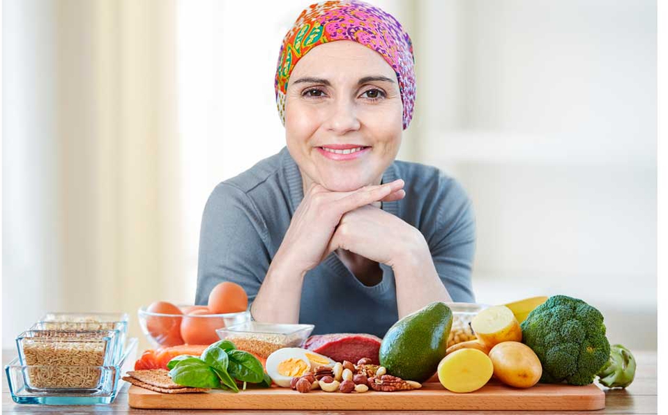 Mujer con tratamiento de cáncer con un montón de aliemtnos sanos sobre tabla de madera